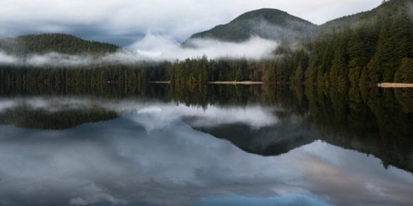 Mountains, clouds and pine trees reflected in a lake.