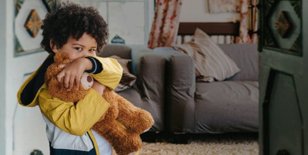 Little boy holding teddybear standing in room.