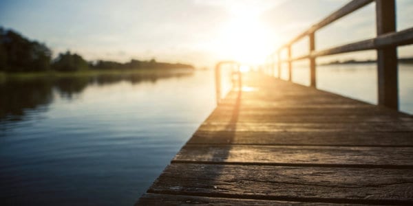 Dock at lake with sun just above the horizon.