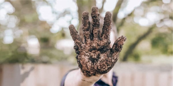 Man holding up hand covered in mud.