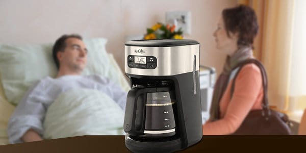 Woman visiting man lying in hospital bed with coffee machine in foreground.
