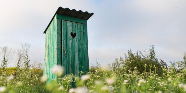Green outhouse in a field.