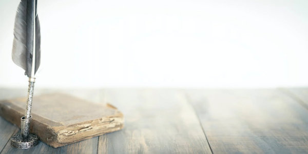 Old book with quill pen on wooden table