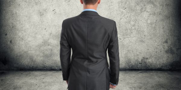 Man in a suit in front of a gray floor and wall