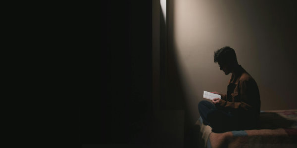 Man sitting on a bed reading a book.