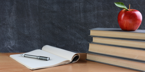 Pile of books with an apple on top in front of a blackboard